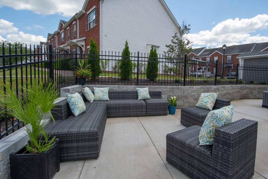 A patio with a black fence and grey wicker furniture.
