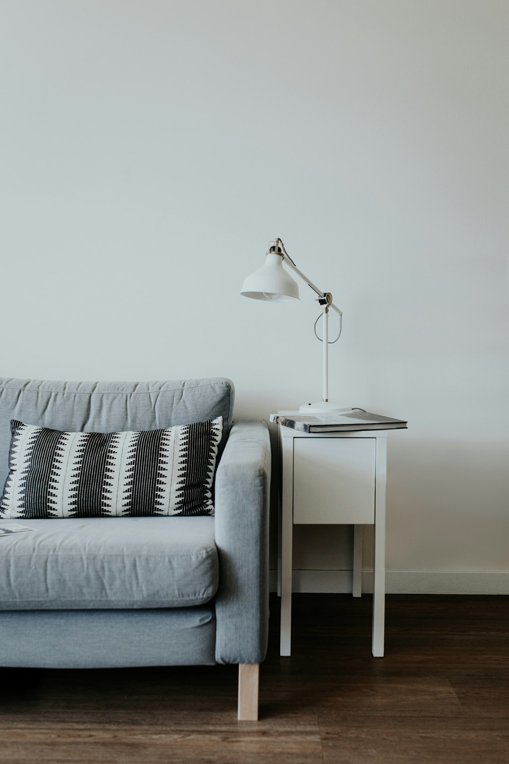 A grey couch with a white table and lamp beside it.