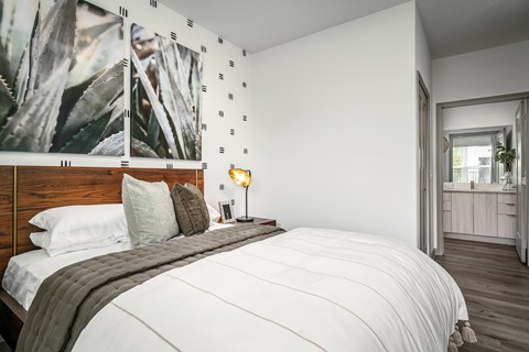 A bedroom with a large bed and a painting of a plant on the wall.