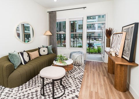 A living room with a green couch and a round mirror on the wall.