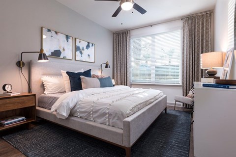 A bedroom with a large bed, a ceiling fan, and a window with curtains.