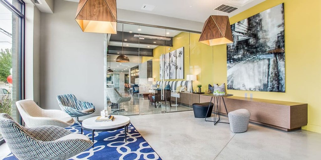 A modern living room with a blue patterned rug and a large abstract painting on the wall.