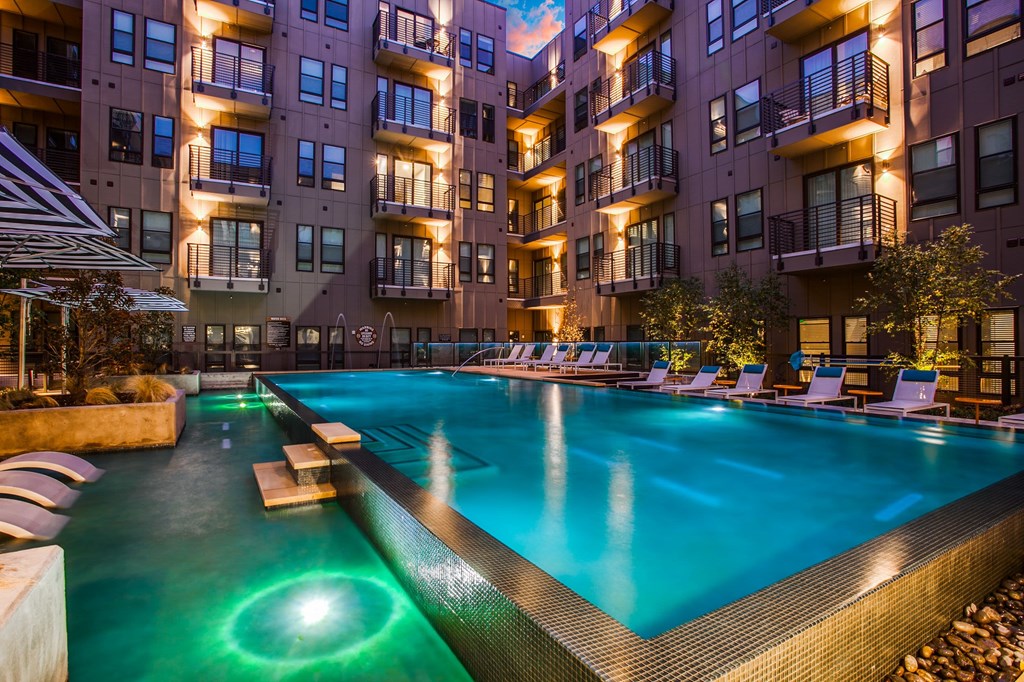 A swimming pool in front of apartment buildings at dusk.
