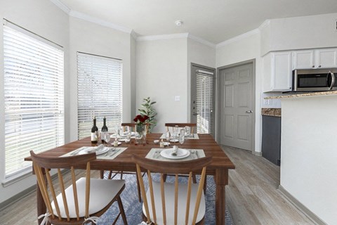 A dining room with a table set for two with a view of a kitchen in the background.