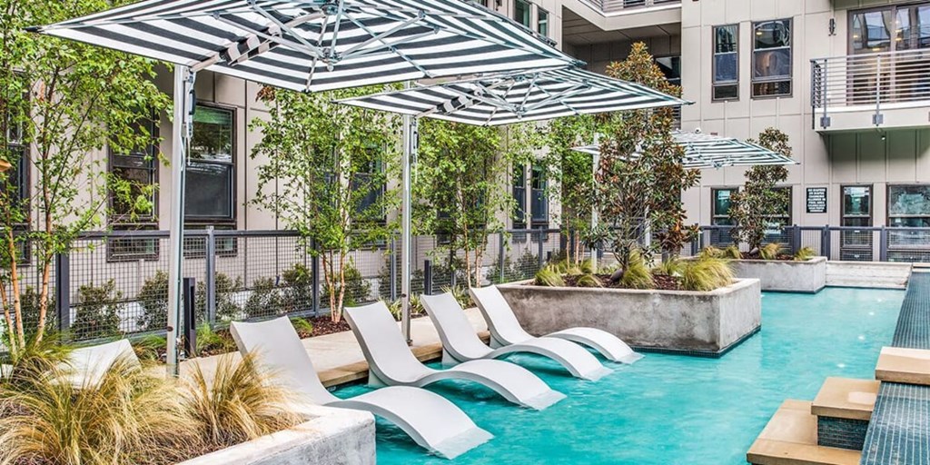 A pool with a striped umbrella and lounge chairs.