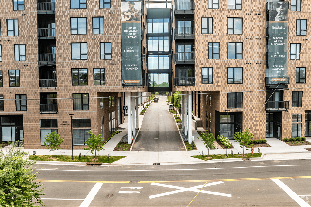 A street view of a residential area with apartment buildings on both sides and a pedestrian crossing in the foreground.