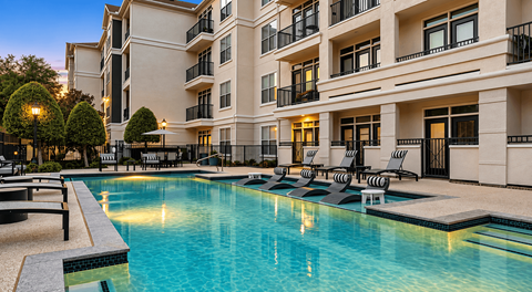 A large swimming pool in front of a building with lounge chairs around it.