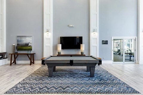 A pool table in the middle of a room with a television and a painting on the wall.