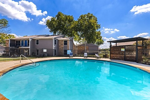 A swimming pool in front of a building with a blue sky and clouds in the background.