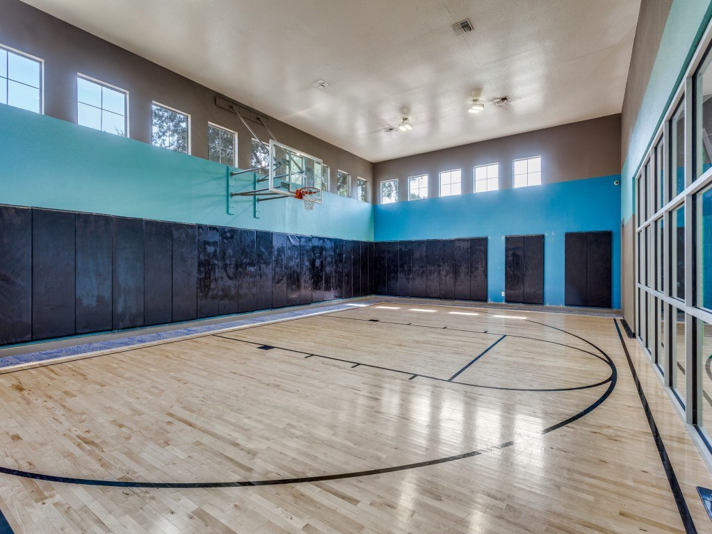 A basketball court inside a gym with a wooden floor and a basketball hoop.
