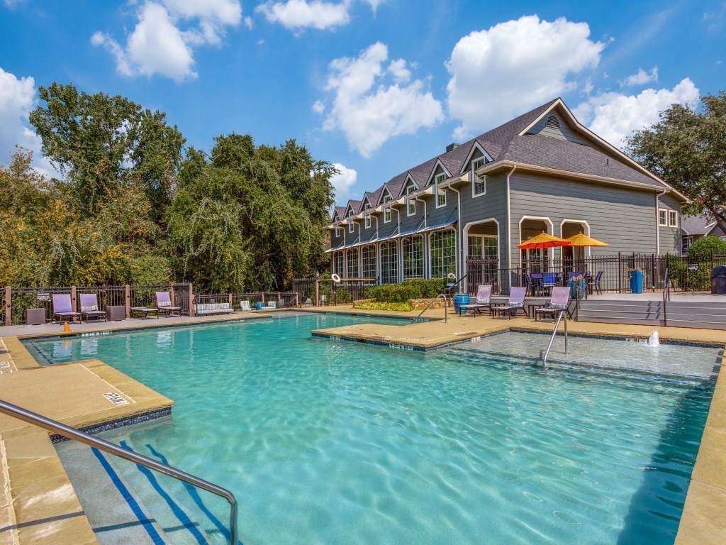 A large swimming pool in front of a building with a blue sky and clouds in the background.