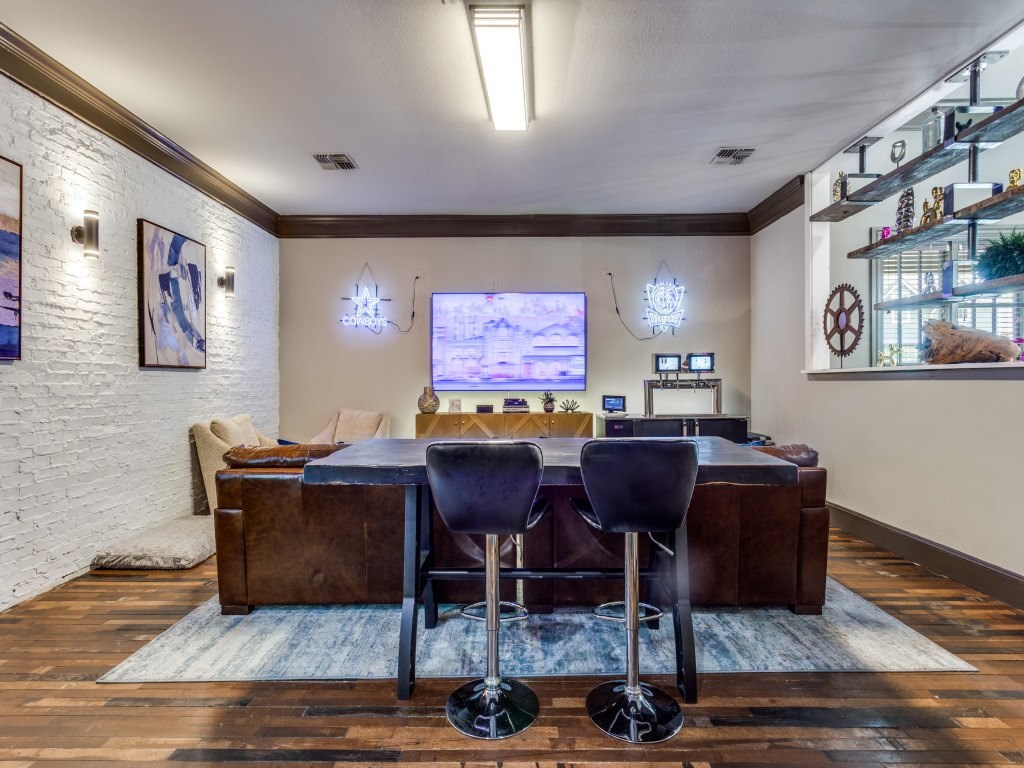 A room with a brown table and chairs with a television in the background.