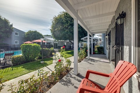 A red chair sits on a patio with a pool and trees in the background.
