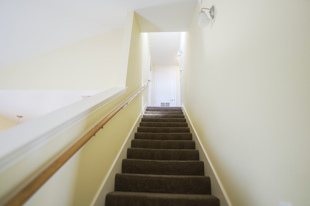A staircase with a brown carpeted runner and white walls.