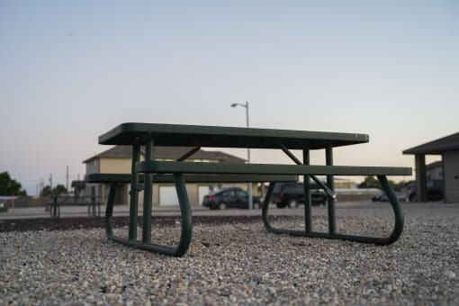 A green picnic table is on a gravel surface.