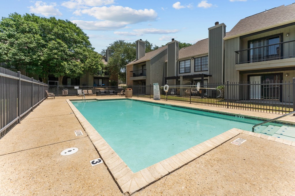 A swimming pool surrounded by a fence and a building in the background.