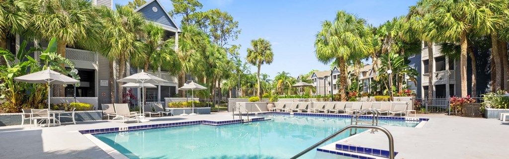 a large swimming pool with chaise lounge chairs and palm trees in front of a building