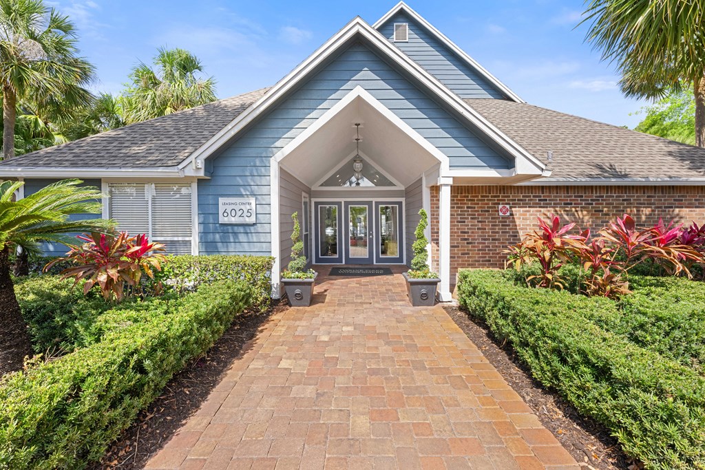 the front of a blue house with a brick walkway and manicured gardens