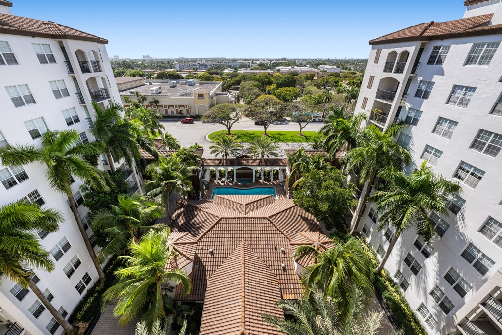 A view from above of a courtyard surrounded by buildings with a pool and palm trees.