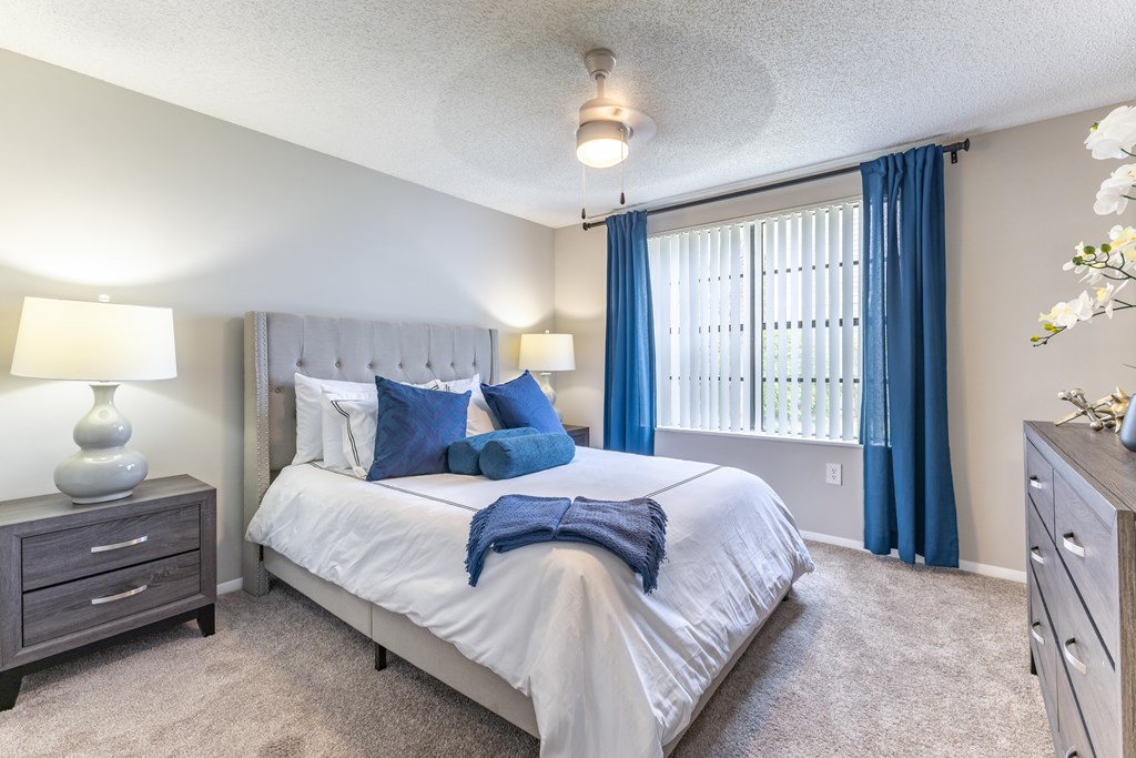 A bedroom with a large bed, a nightstand, and a window with blue curtains.