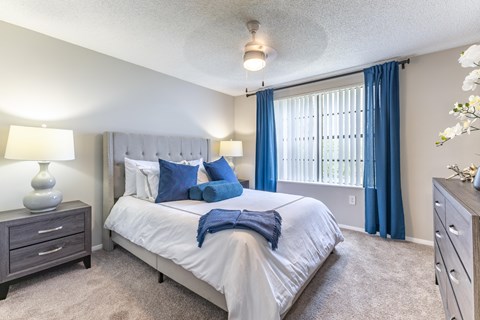A bedroom with a large bed, a nightstand, and a window with blue curtains.