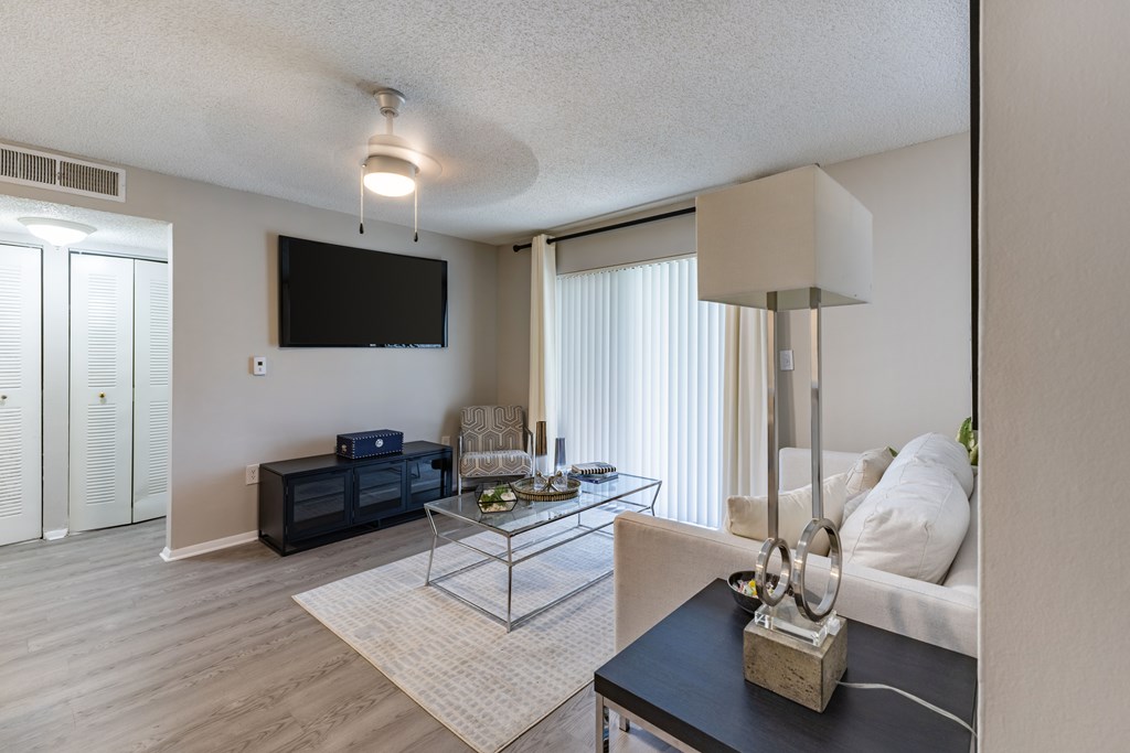 A living room with a black sofa, a glass coffee table, and a television mounted on the wall.