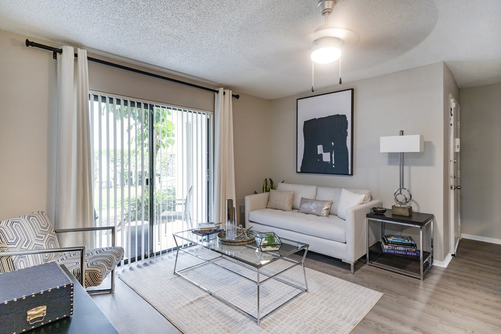 A living room with a white couch, a coffee table, and a large window with curtains.
