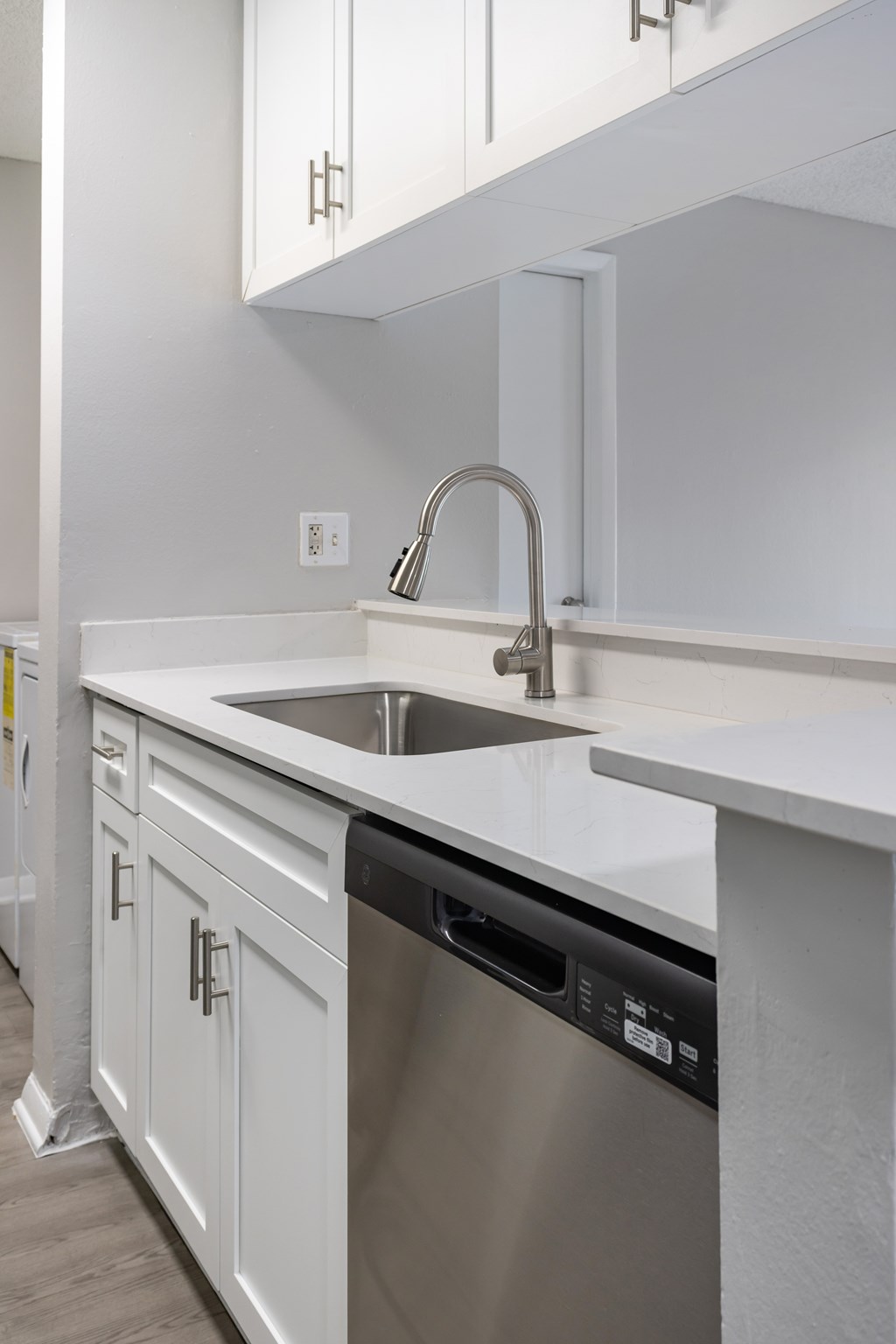 A modern kitchen with a stainless steel dishwasher and white countertops.