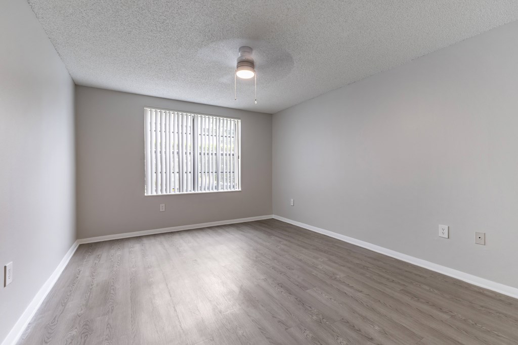 A room with a window covered by blinds and wooden flooring.