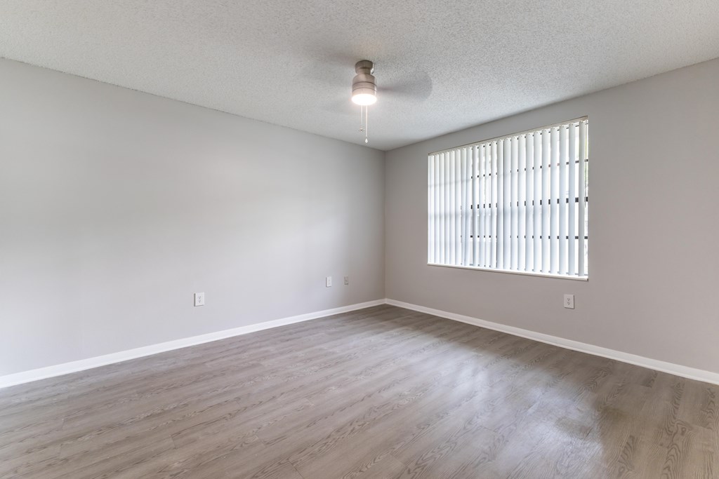 A room with a window covered by blinds and wooden flooring.