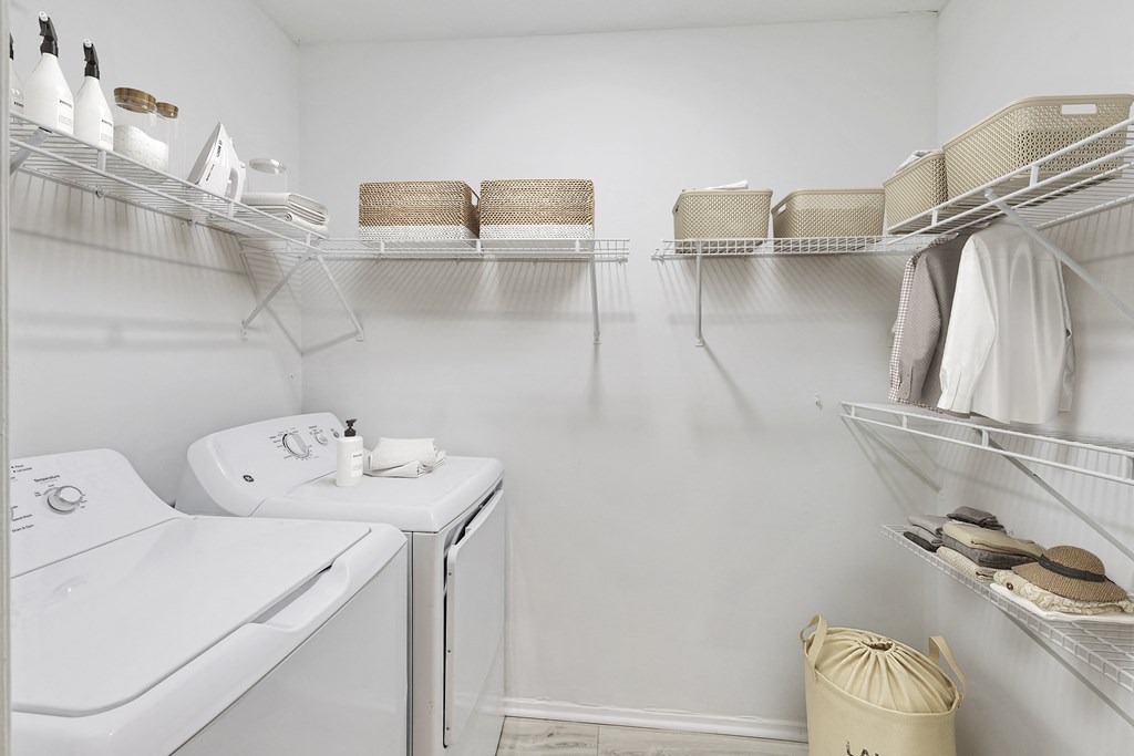 a white laundry room with a washer and dryer and shelves with baskets