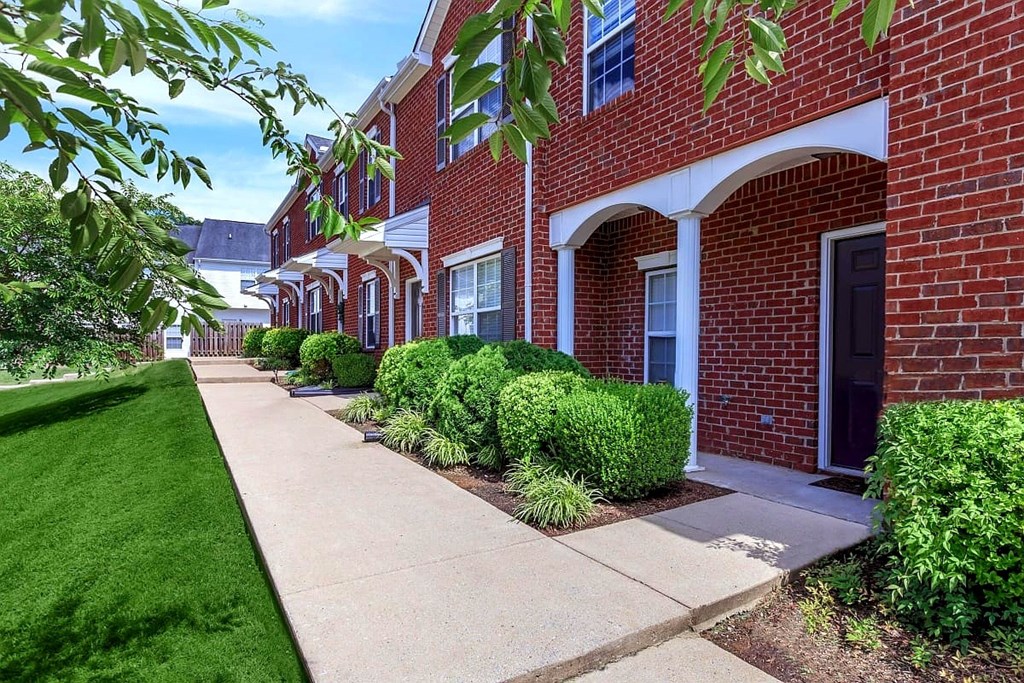 A row of red brick houses with green bushes in front.
