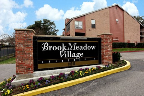 a sign for brook meadow village in front of a brick building