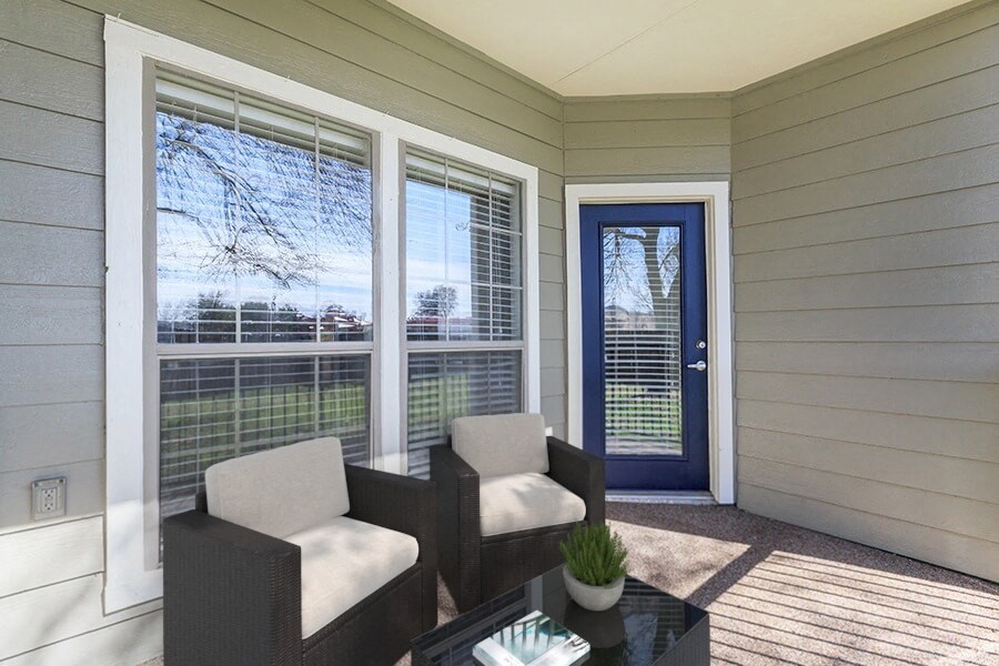 A sunny day outside a house with a blue door and a glass table with two chairs.