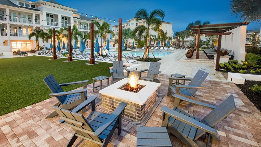 a patio with a firepit and chairs and a pool in the background