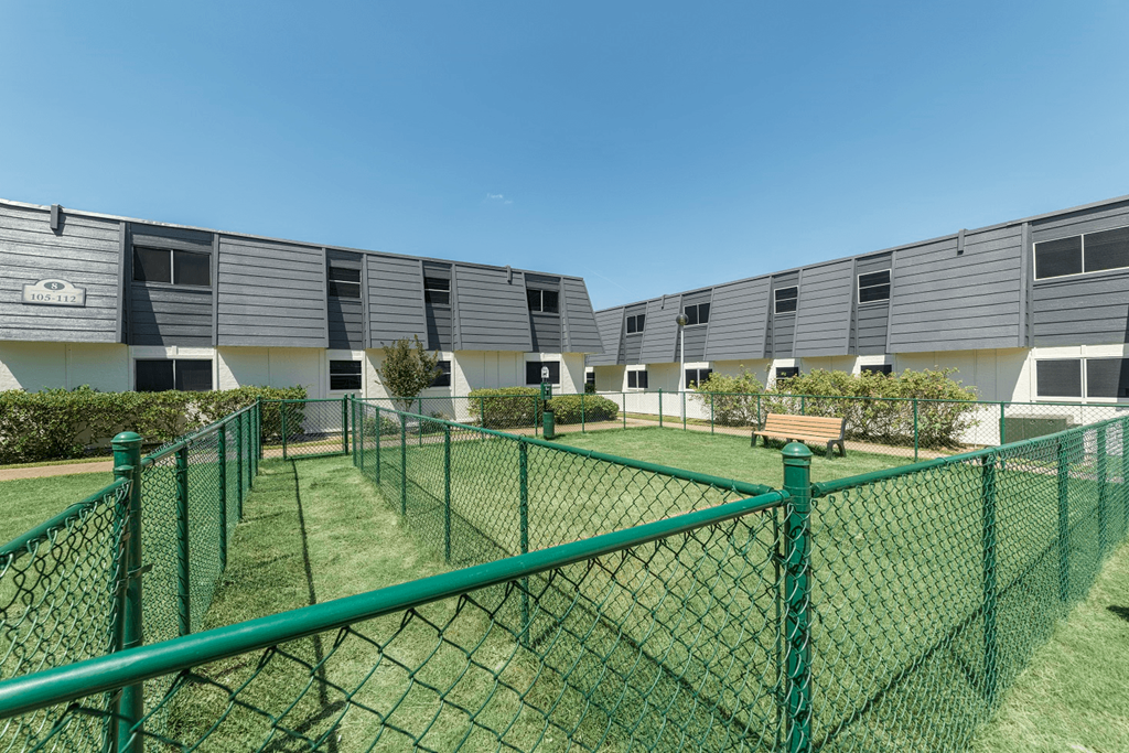 a row of apartment buildings with green fencing and a grass yard