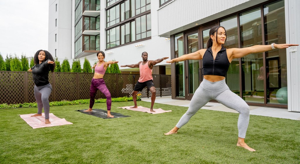 Four people are practicing yoga on a grassy area in front of a building.
