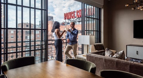 A man and woman standing in a room with a large window that has a view of a building with the word "Ponce" on it.