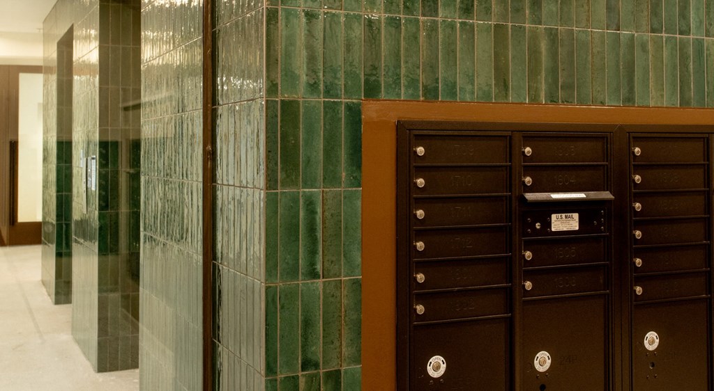 A brown mailbox is in front of a green tiled wall.
