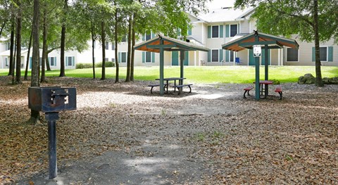 A park with picnic tables and benches in front of apartment buildings.
