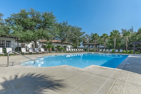 A large swimming pool surrounded by trees and lounge chairs.