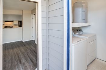 A white washing machine is in a kitchen with white cabinets.