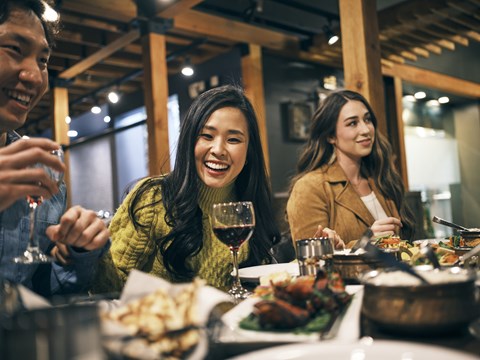 Three people are sitting at a table with food and drinks.