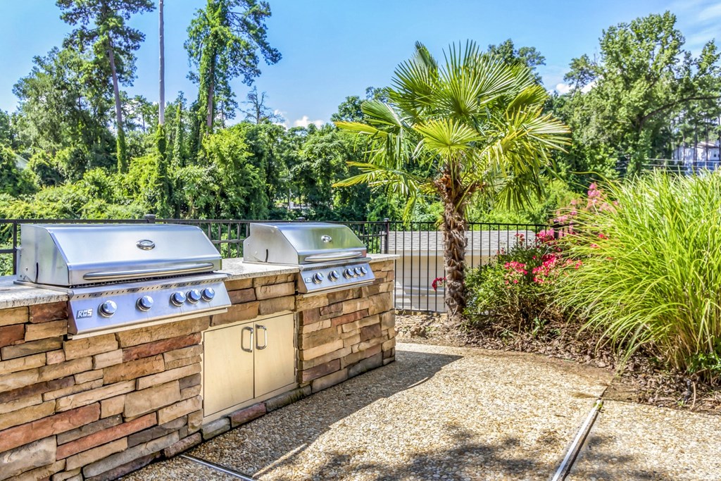 two gas grills on a brick wall in a backyard with trees