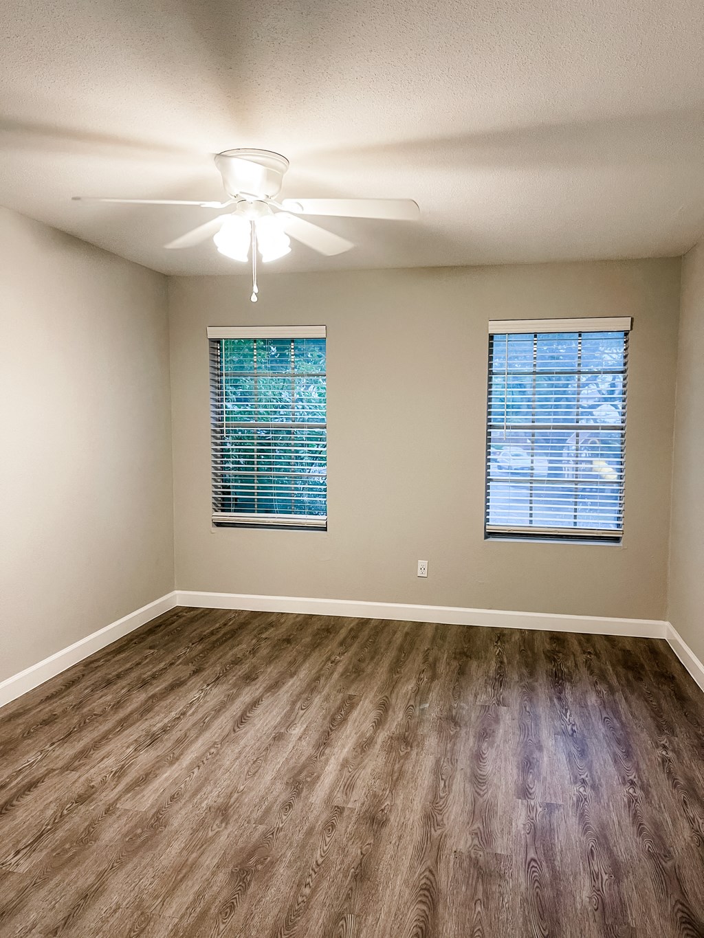 an empty bedroom with two windows with wood flooring