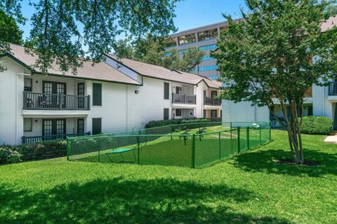 A sunny day at a green, grassy courtyard with a tennis court and apartment buildings in the background.
