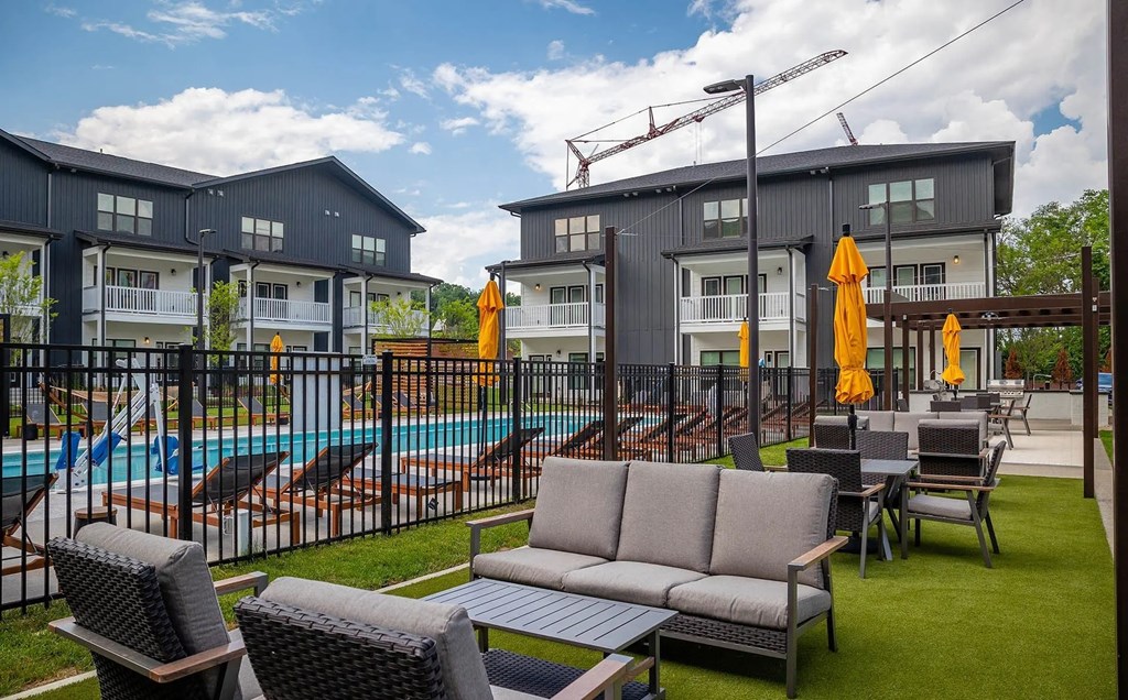 A poolside area with chairs, a sofa, and umbrellas in front of a building.
