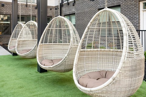 Three white hanging egg chairs with cushions are suspended from a metal frame.
