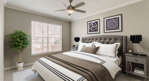 A bedroom with a large bed, a ceiling fan, and a potted plant.