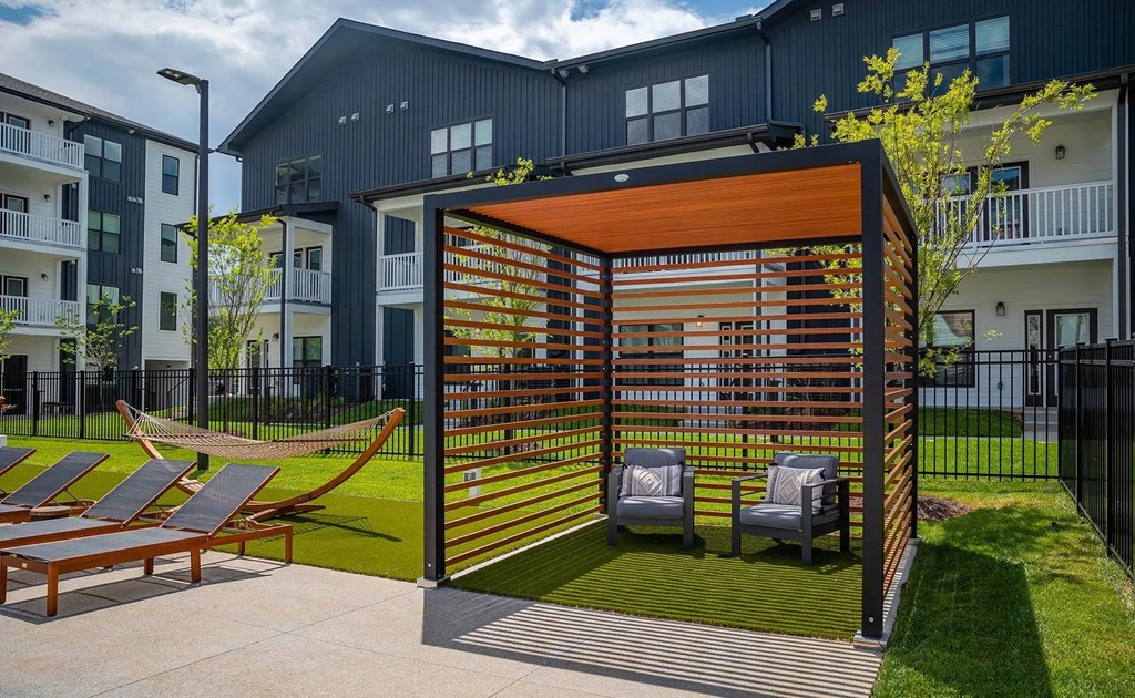A patio with a hammock and chairs is surrounded by a black fence.